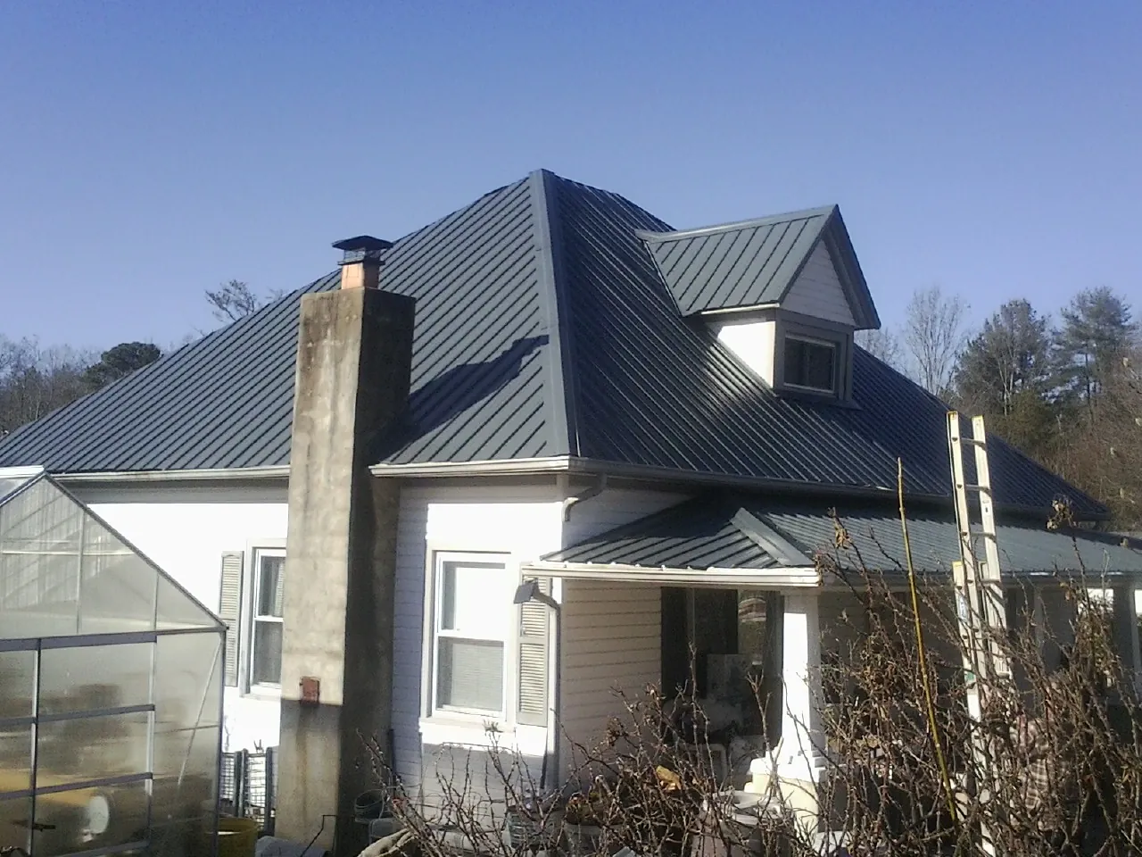 Dark blue standing seam metal roof on a white farmhouse with dormer — Slate & Tile Roof Repair by Roofing Brothers in Great River