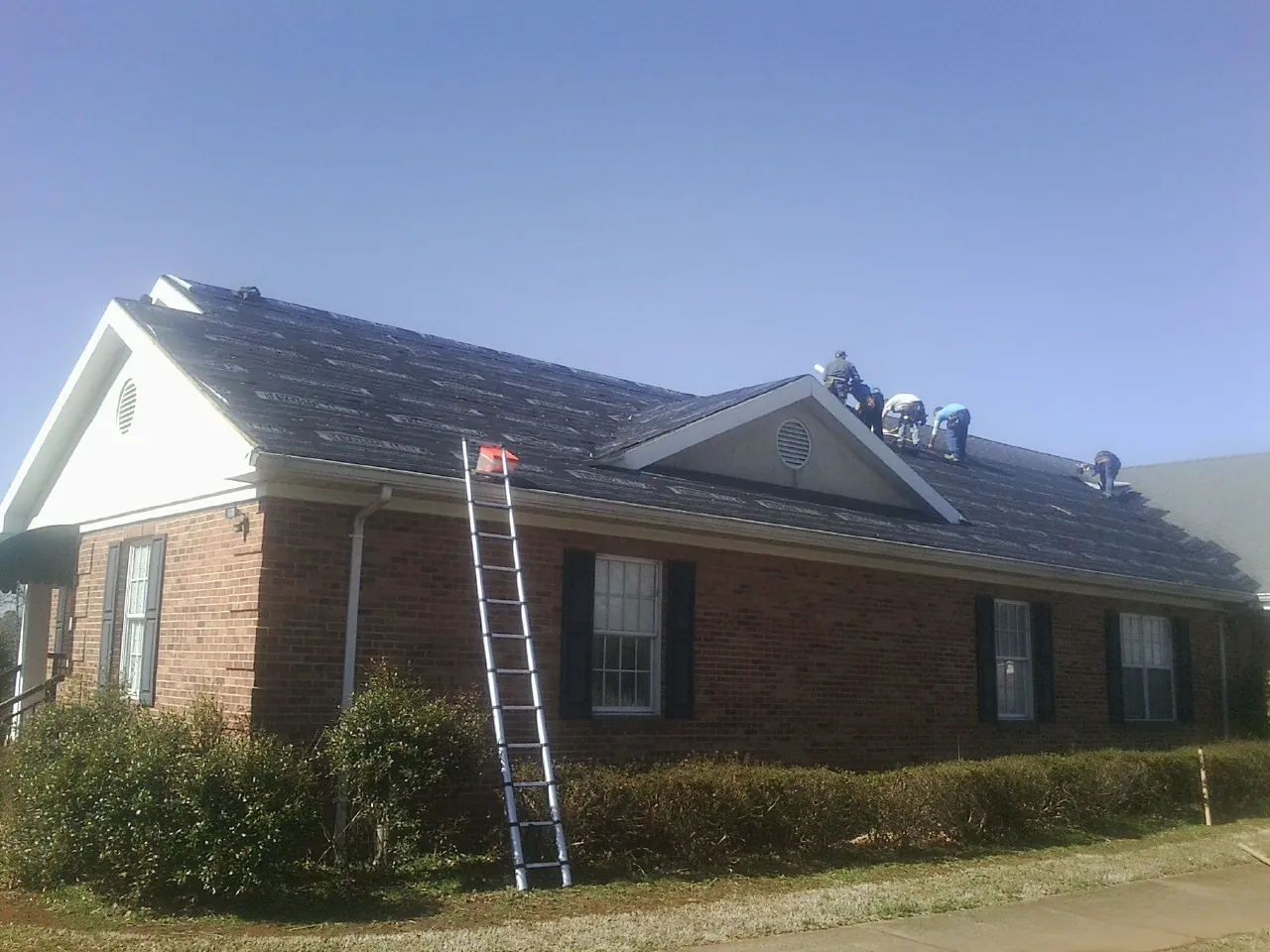 Crew tearing shingles off a brick ranch roof with a ladder set — Emergency Roof Repair work by our crew in Great River
