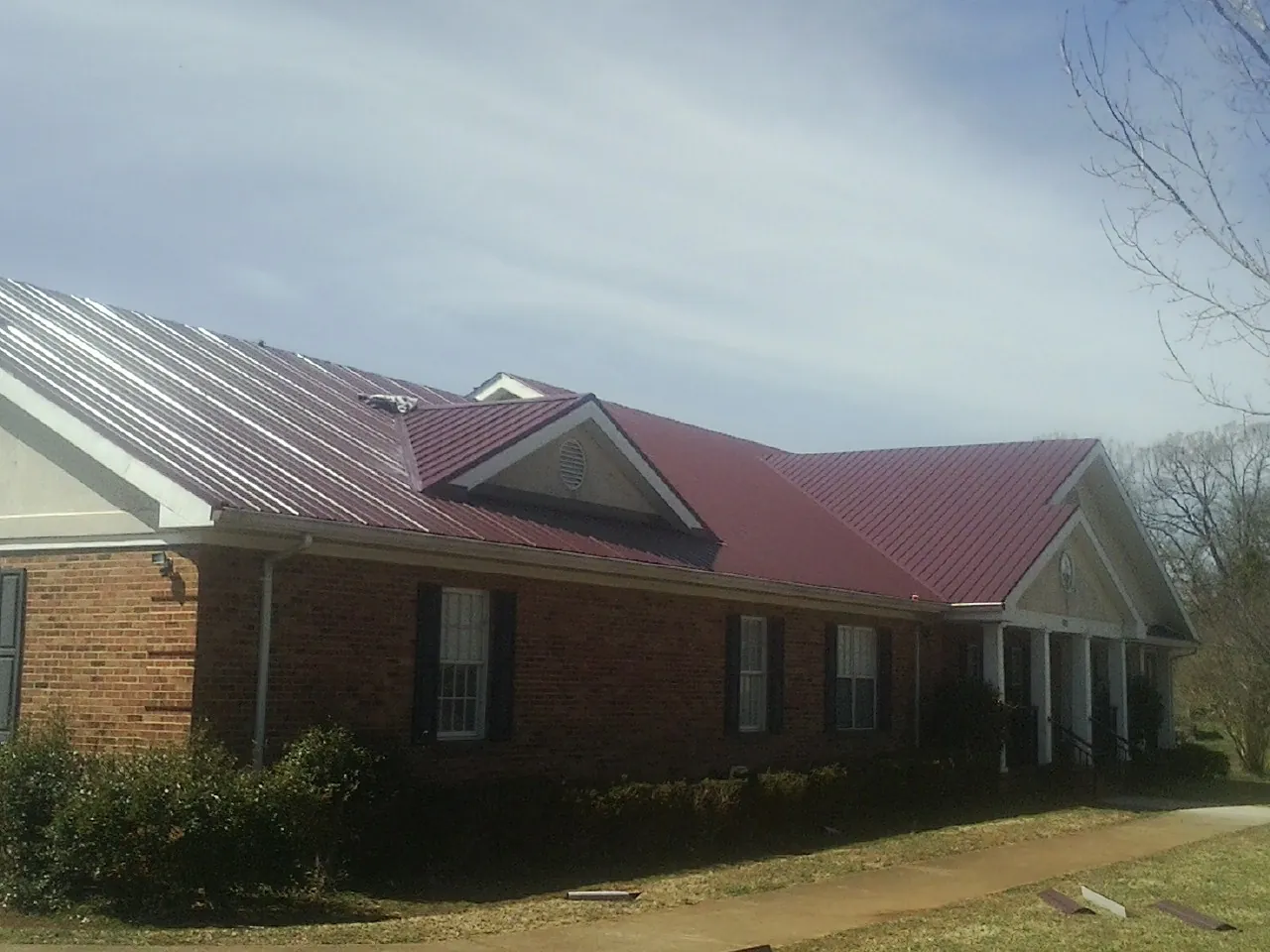 Red metal roof with gabled entries on a long brick building, from a Hail Damage Roof Repair job in Great River