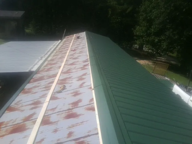Old rusted panels beside newly installed green metal roofing — Wind Damage Roof Repair by Roofing Brothers in Great River