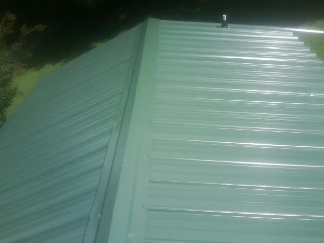 New green metal panels meeting at the ridge of a roof — Flat Roof Repair work by our crew in Great River