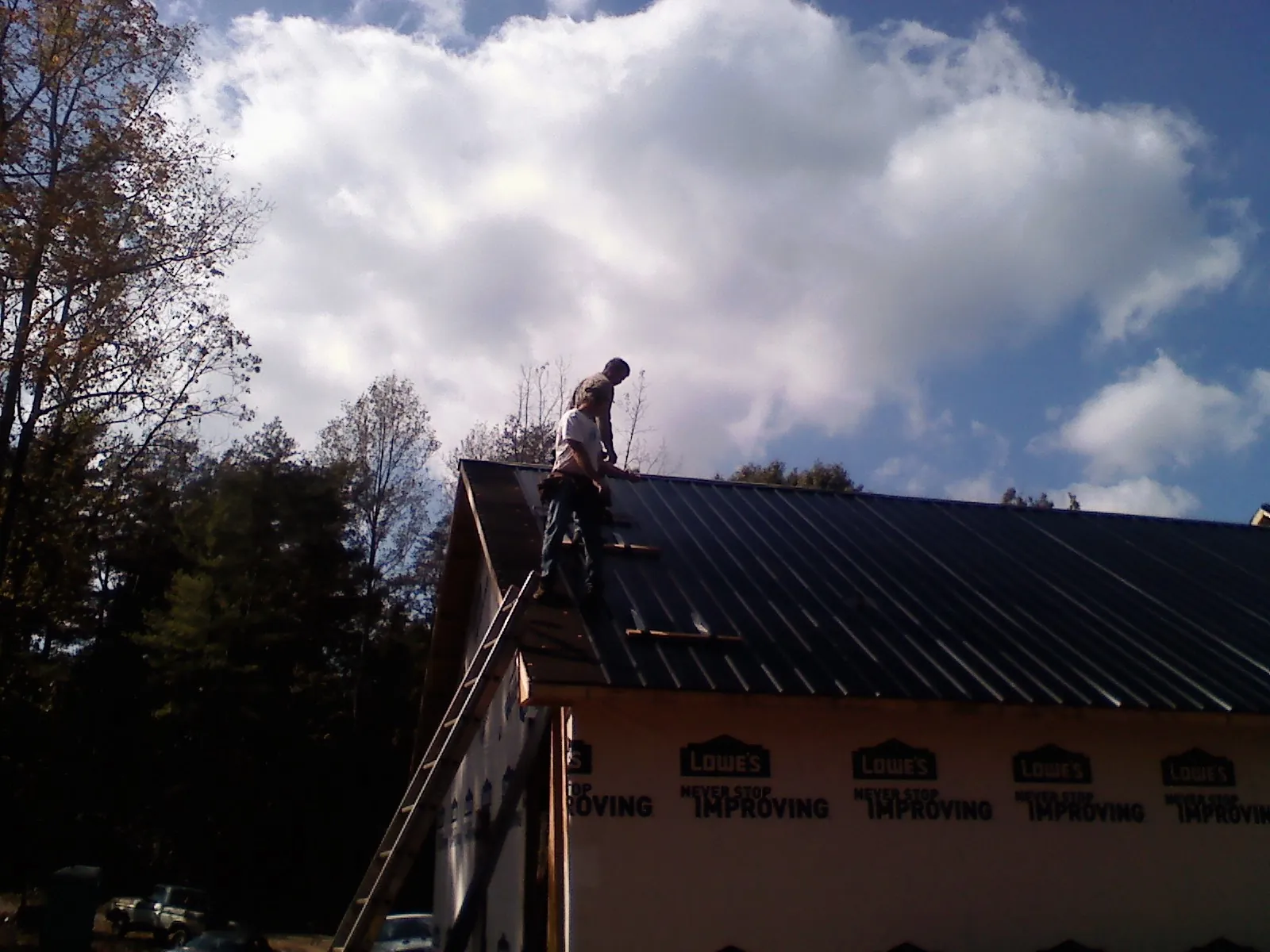 Roofer fastening dark metal panels high against a cloudy sky, from a Roof Inspection job in Great River