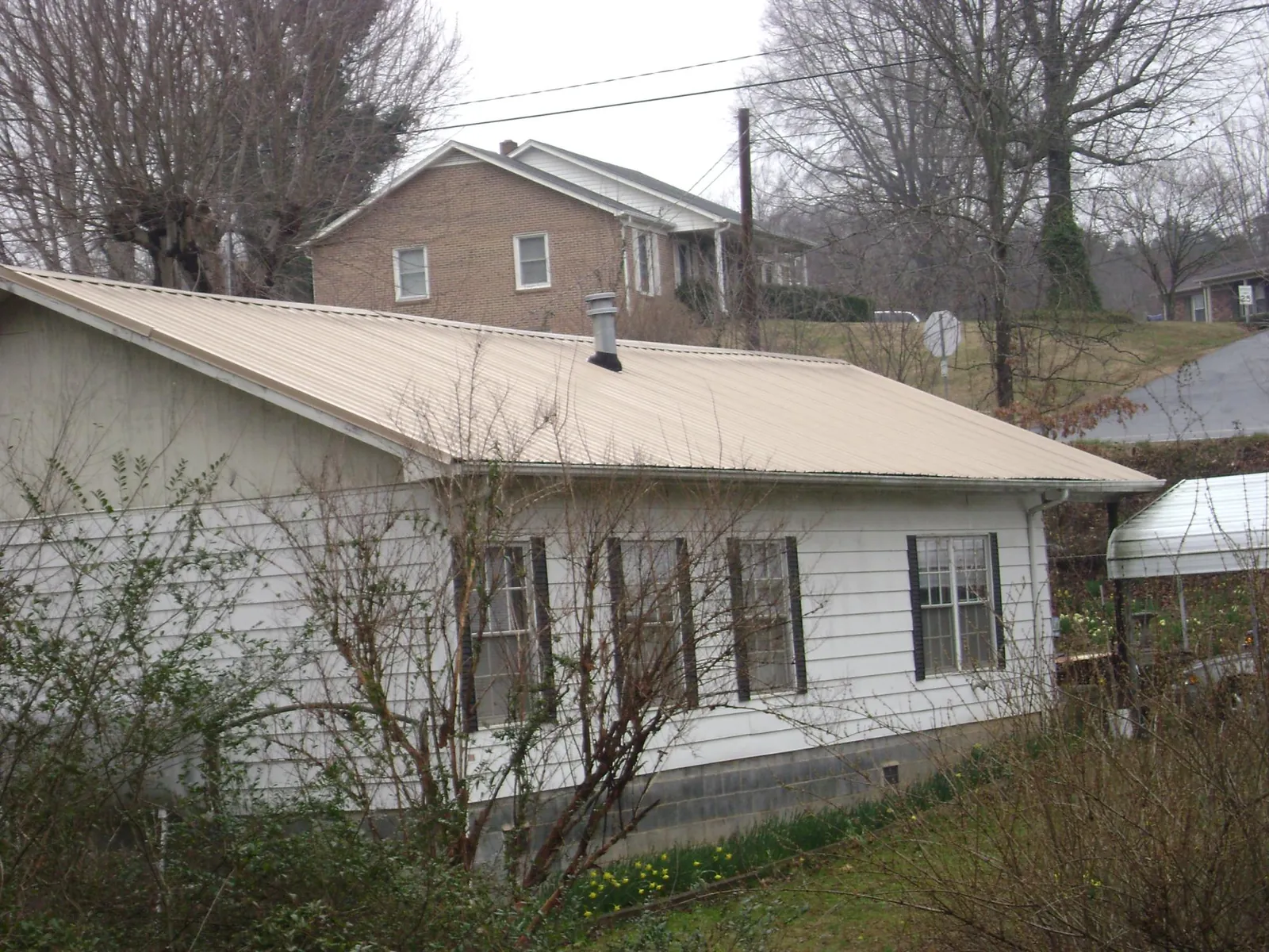 Tan metal roof on a white sided house set into a hillside — Commercial Roofing by Roofing Brothers in Great River