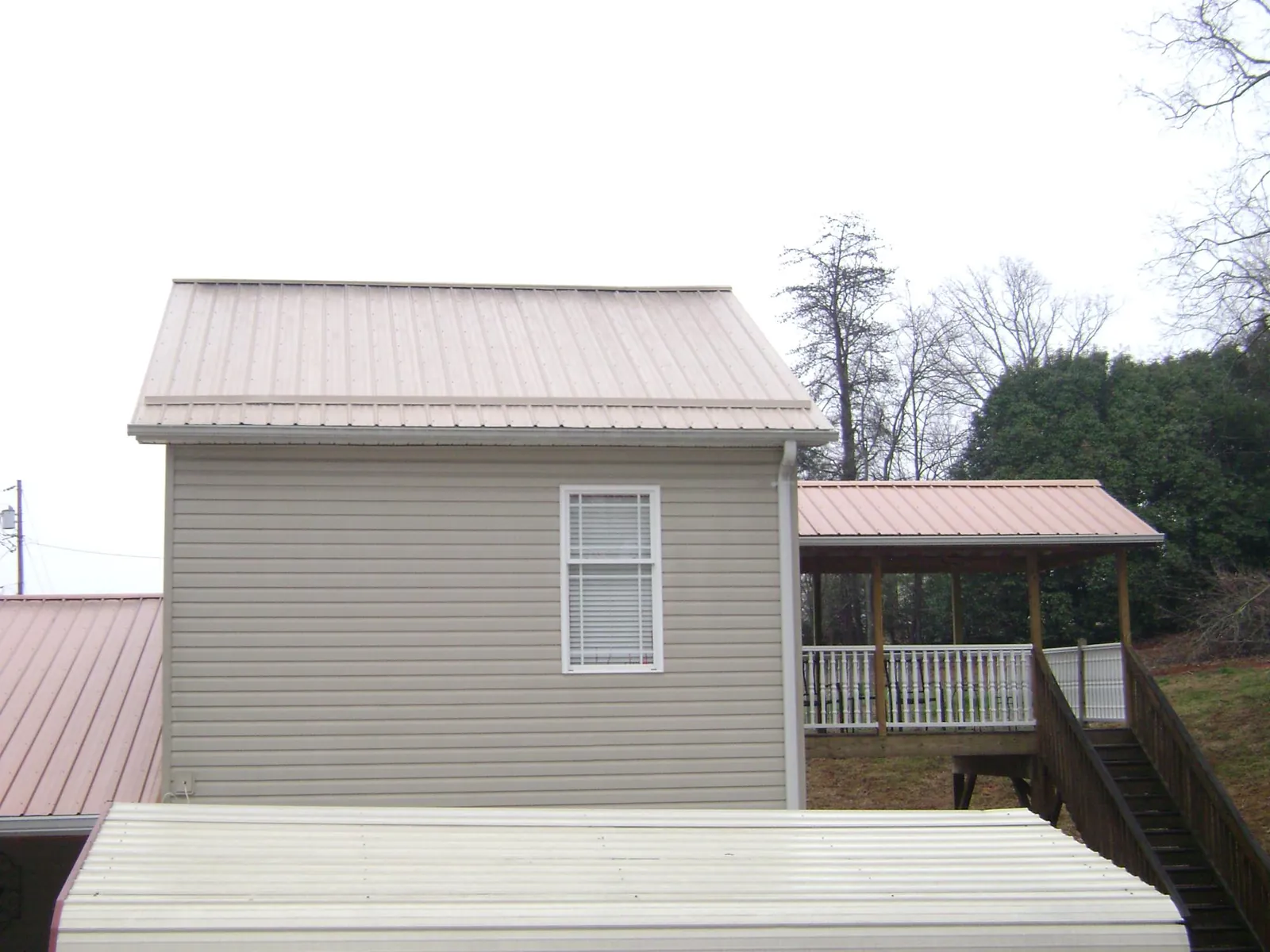 Tan metal roofs on a two story addition and attached porch, from a Roof Replacement job in Great River